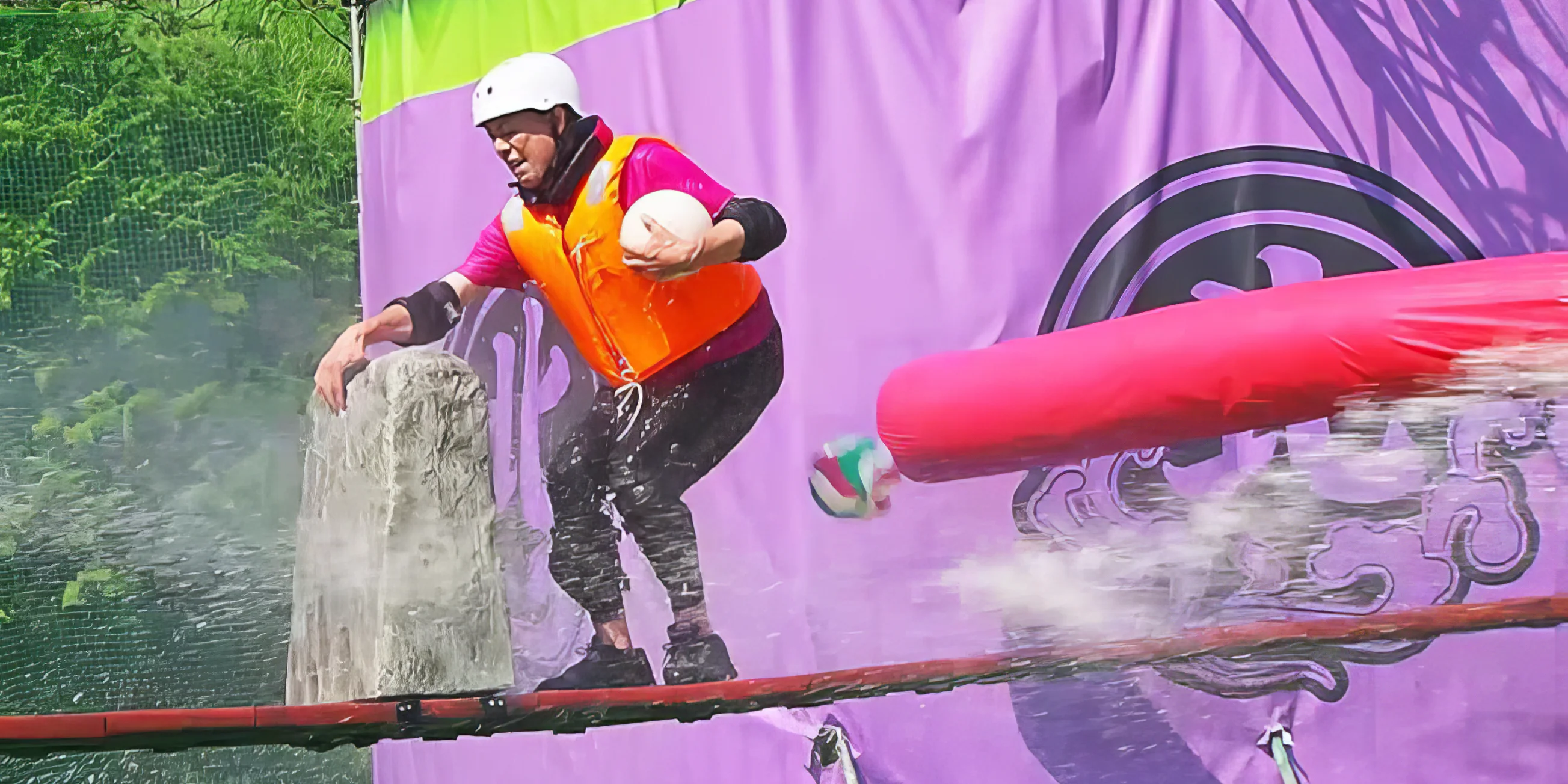 A contestant on a narrow bridge trying to avoid a water cannon, flying ball and rotating arm